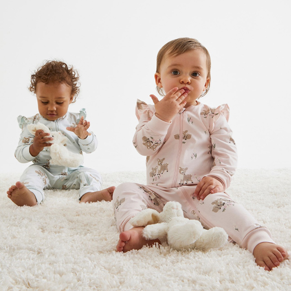 Två toddlers sitter på en fluffig matta klädda i mönstrad babypyjamas